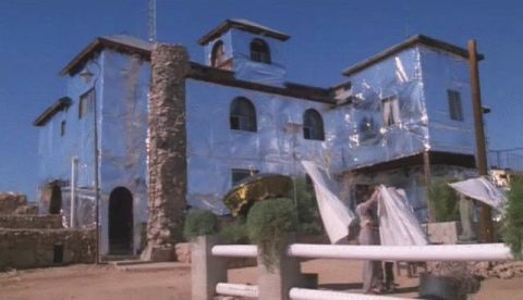 1990 Ford Bronco - Video still of a large stucco house wrapped head-to-toe in reflective foil sheeting under a blue sky, with people holding up more foil in t…