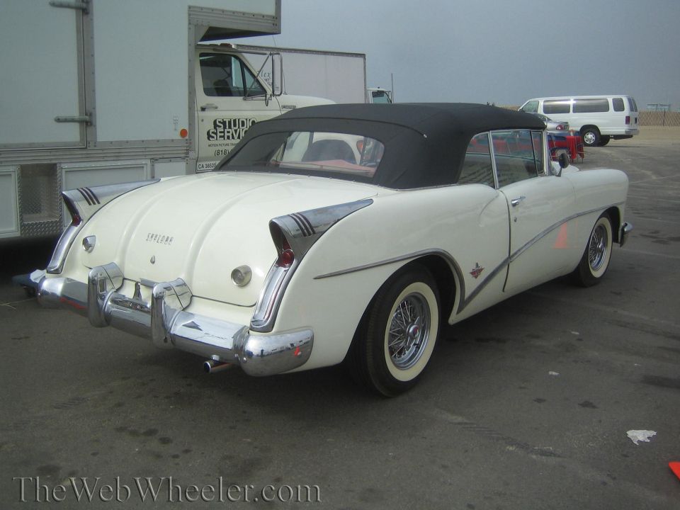 Rear three-quarter view of a white 1950s convertible with black top and wire wheels