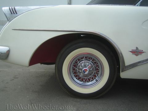1990 Ford Bronco - Close-up of a white classic car's front fender, chrome trim and red-painted wheel well with a chrome wire wheel and whitewall tire.