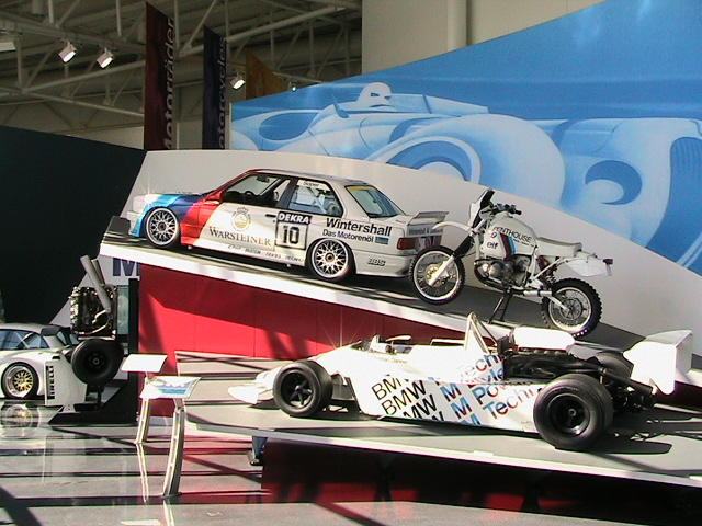 BMW museum display with white race sedan, rally motorcycle, and BMW formula car