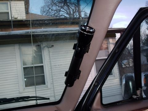 1996 Ford Bronco - A black flashlight is mounted on the A-pillar inside a vehicle, with a residential house seen through the windows.