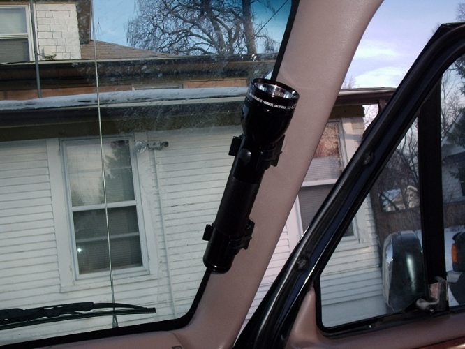 Flashlight mounted on interior pillar of a vehicle, with a house visible through the windshield