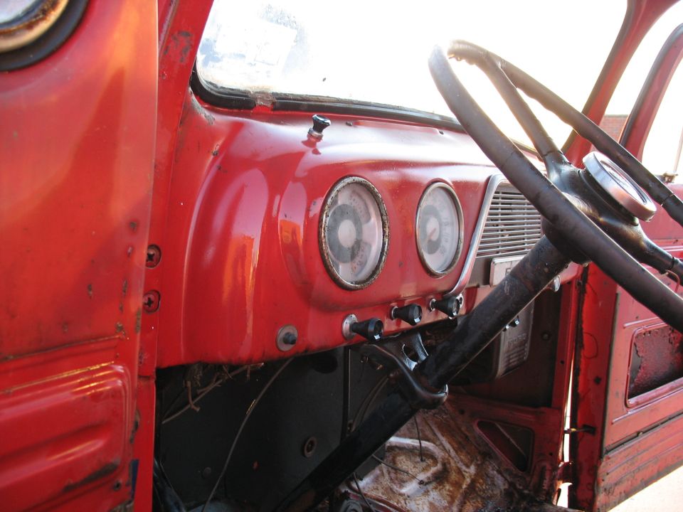 Red truck dashboard with two circular gauges, black steering wheel, and red door panel
