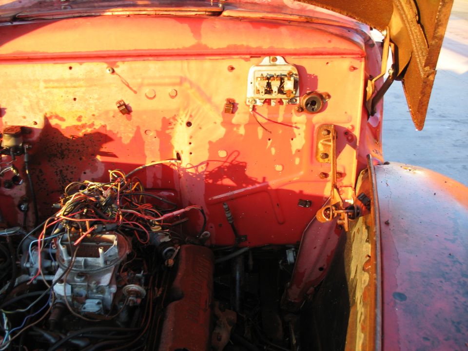 Red truck engine bay with exposed wires and a carburetor