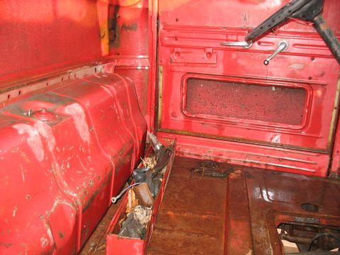 1952 Ford Pickup - The interior of a vintage truck shows a red cab with a large fuel tank and a toolbox filled with various items.