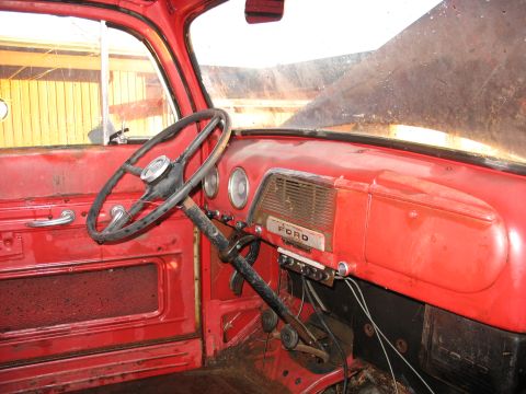 1952 Ford Pickup - The interior of a red Ford pickup truck shows a dashboard with a prominent Ford logo and a two-spoke steering wheel.