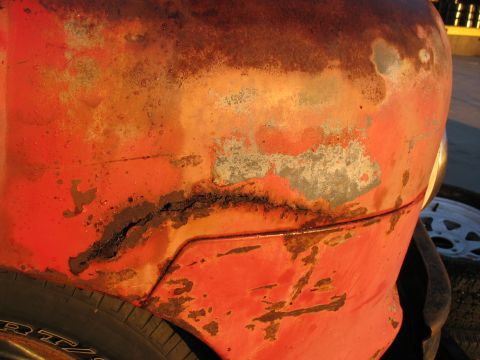 1952 Ford Pickup - The heavily rusted fender of a 1952 Ford Pickup shows significant wear and tear, with a prominent crack along a body line.