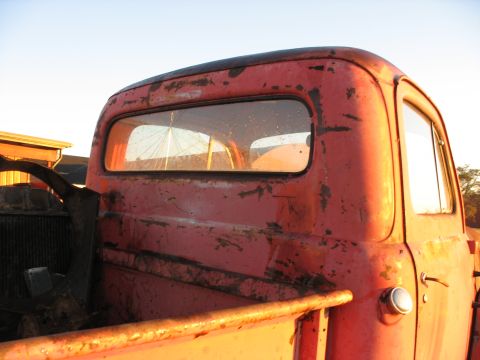 1952 Ford Pickup - A weathered red pickup truck cab, seen from the rear, with visible rust and damage.