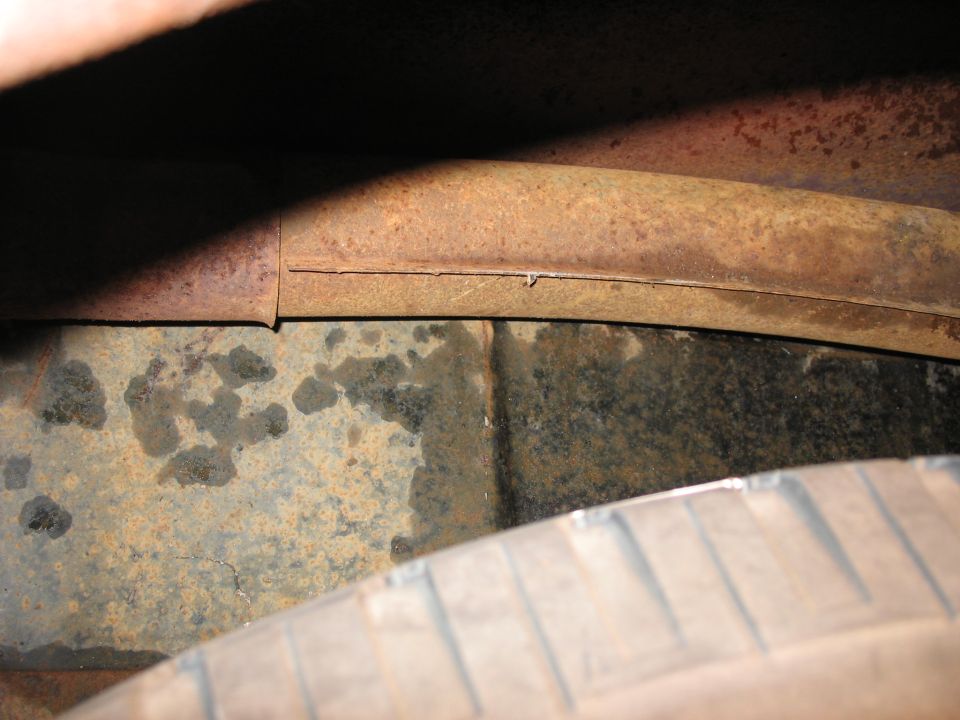 rusted frame rail above a tire and wet undercarriage