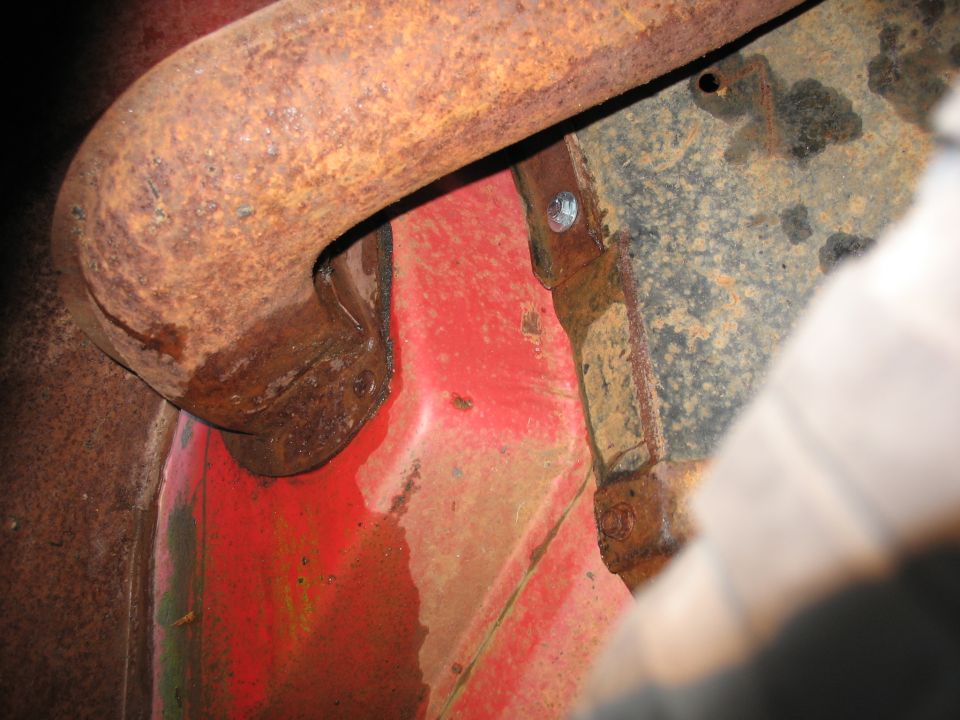 Close-up of a rusted exhaust pipe over red painted metal with visible water stains and dirt