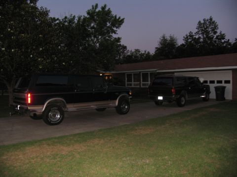 1995 Ford C-350 (Centurion Conversions) - A long, black SUV and a shorter SUV are parked in a driveway in front of a house and garage.