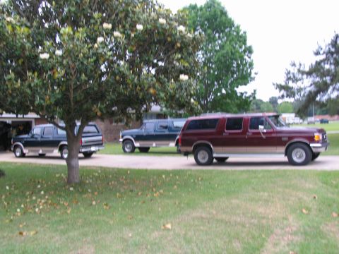 1995 Ford C-350 (Centurion Conversions) - Three extended SUVs are parked in a residential driveway under trees.