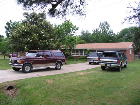 1995 Ford C-350 (Centurion Conversions) - A maroon SUV with tan trim is parked on a driveway in front of a house, with two other SUVs behind it.