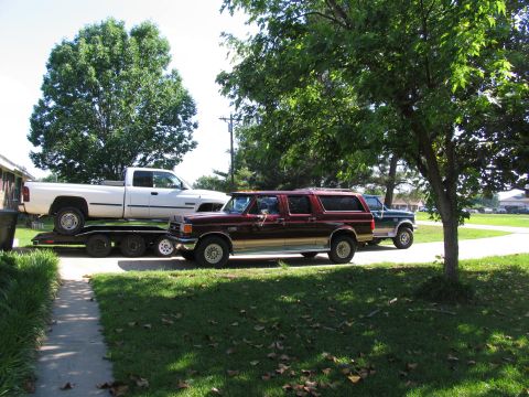 1995 Ford C-350 (Centurion Conversions) - Three vehicles are parked outside on a sunny day, with a white pickup truck loaded onto a trailer.