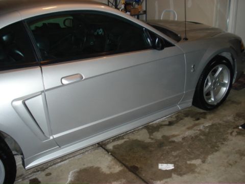 1998 Ford Taurus - A silver Ford Mustang is parked in a garage, its side profile and front wheel clearly visible.