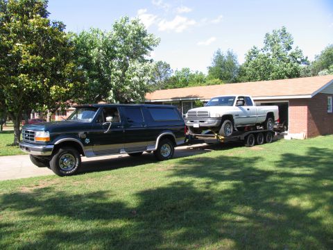 1995 Ford C-350 (Centurion Conversions) - A Ford Bronco SUV tows a Dodge Ram pickup truck on a trailer, parked in a driveway.