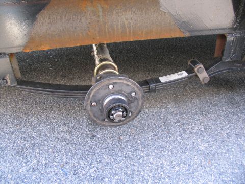 1995 Ford C-350 (Centurion Conversions) - The underside of a trailer shows a single axle with its suspension system, including leaf springs and a wheel hub.