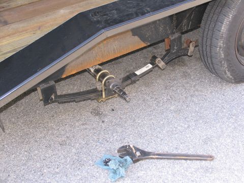 1995 Ford C-350 (Centurion Conversions) - Close-up of a trailer's suspension system, showing leaf springs and a spindle, with a wrench nearby.