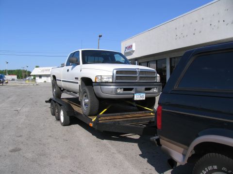 1995 Ford C-350 (Centurion Conversions) - A white pickup truck is loaded onto a trailer, with another vehicle partially visible in the foreground.