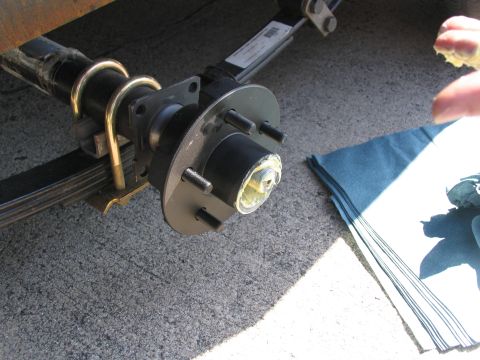 1995 Ford C-350 (Centurion Conversions) - Close-up of a trailer axle hub assembly being greased, with a leaf spring and U-bolts visible.