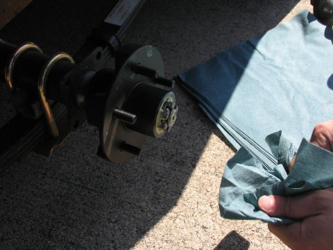 1995 Ford C-350 (Centurion Conversions) - Close-up of a trailer's axle and wheel hub assembly, with a hand holding a cleaning cloth.