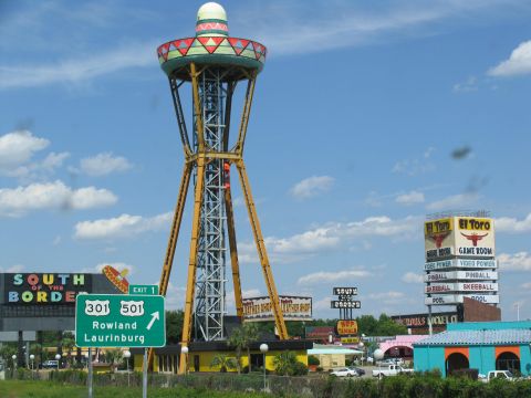 1995 Ford C-350 (Centurion Conversions) - South of the Border attraction with its iconic sombrero tower and various roadside businesses under a partly cloudy sky.