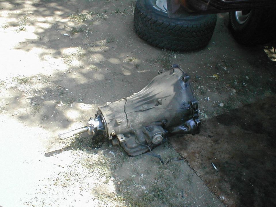 Removed automatic transmission sitting on the ground beside a tire in a yard