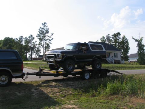 1995 Ford C-350 (Centurion Conversions) - A dark blue Ford Bronco is loaded onto a trailer, with another dark vehicle visible in the foreground.