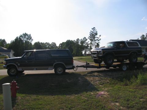 1995 Ford C-350 (Centurion Conversions) - A black Ford Bronco is transported on a trailer pulled by a dark-colored Ford Econoline van.