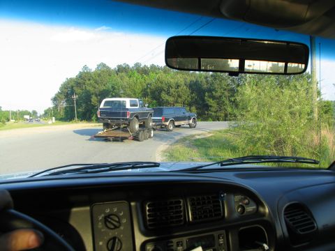 1995 Ford C-350 (Centurion Conversions) - A Ford Bronco is transported on a trailer, pulled by a Ford Excursion on a rural road.