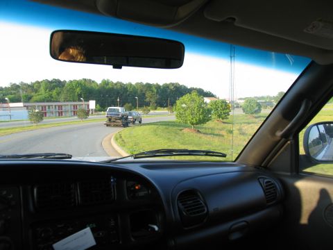 1995 Ford C-350 (Centurion Conversions) - A truck tows a car on a trailer down a road, seen from the perspective of the towing vehicle's interior.