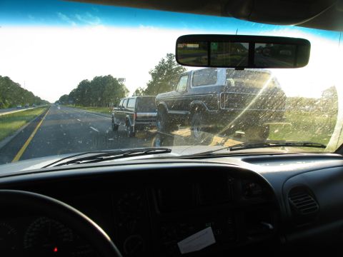 1995 Ford C-350 (Centurion Conversions) - View from inside a vehicle, looking at a trailer carrying a Ford Bronco on the highway.