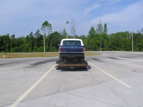 1995 Ford C-350 (Centurion Conversions) - A blue and white pickup truck is seen from the rear, loaded onto a trailer in a parking lot.