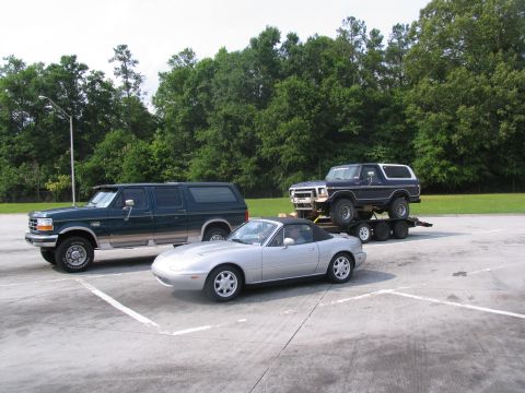 1995 Ford C-350 (Centurion Conversions) - Three vehicles are parked in a lot: a Ford Bronco on a trailer, a Ford Econoline van, and a Mazda Miata convertible.