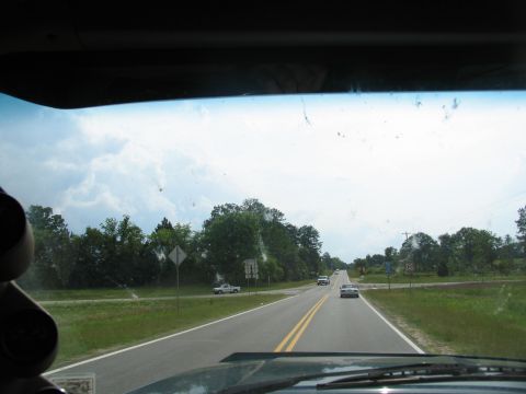 1995 Ford C-350 (Centurion Conversions) - A view from inside a vehicle shows a two-lane road with a white pickup truck and other cars under a cloudy sky.