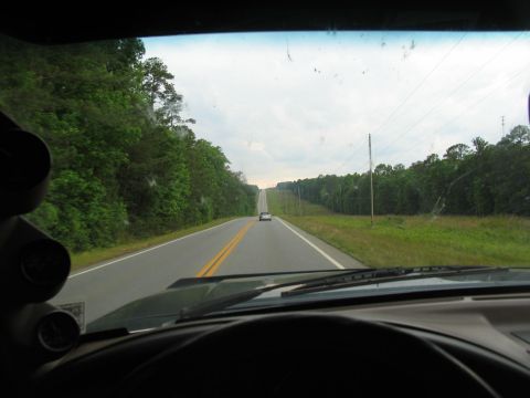1995 Ford C-350 (Centurion Conversions) - Driving down a long, straight road with trees lining both sides and a white car ahead.