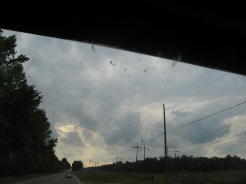 1995 Ford C-350 (Centurion Conversions) - View from a car window shows a rural road with power lines and trees under a cloudy sky.