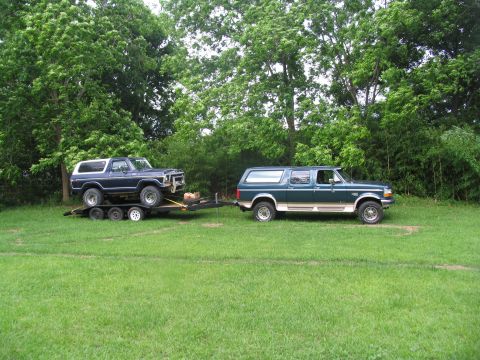 1995 Ford C-350 (Centurion Conversions) - A Ford Bronco is loaded onto a trailer and towed by a Ford Excursion in a grassy area.