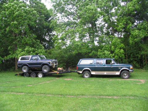 1995 Ford C-350 (Centurion Conversions) - A dark blue Ford Bronco is loaded onto a trailer, which is then towed by a green Ford Econoline SUV.