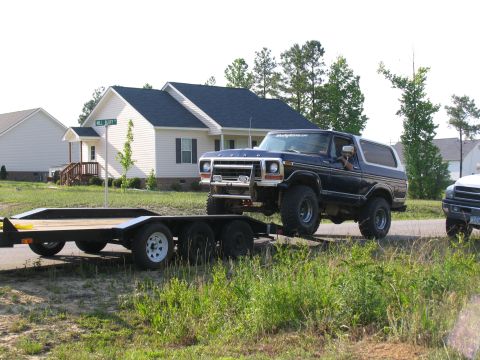 1978 Ford Bronco - A dark blue Ford Bronco is being towed on a trailer down a residential street.