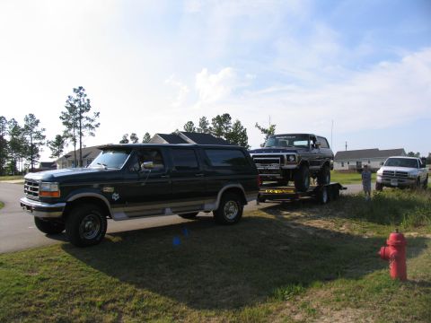 1978 Ford Bronco - A dark blue Ford Bronco is transported on a trailer, with a dark green SUV and a white pickup truck present.
