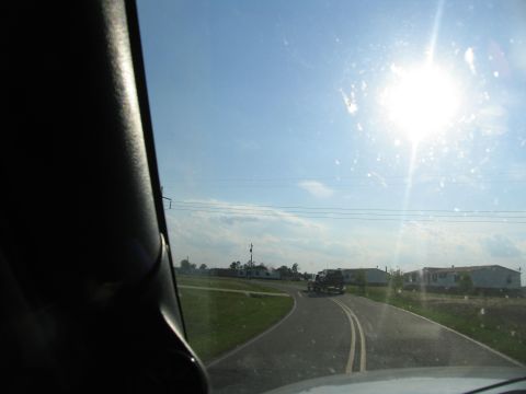 1978 Ford Bronco - A truck tows a trailer down a two-lane road under a bright, sunny sky, with mobile homes visible on the side.