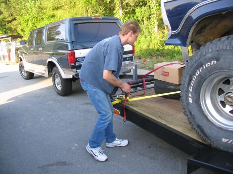 1978 Ford Bronco - A man secures a dark green Ford Bronco with woodgrain trim onto a trailer, with another vehicle visible in the background.