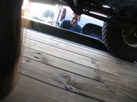 1978 Ford Bronco - A man peers out from beneath a vehicle, with a tire visible on the right side.