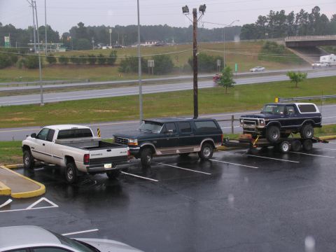 1978 Ford Bronco - A dark blue 1978 Ford Bronco is loaded onto a trailer, parked in a lot with other vehicles.