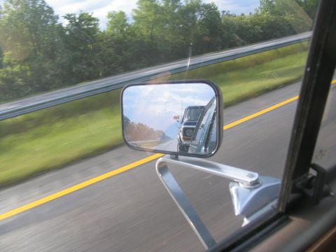 1978 Ford Bronco - View of a dark blue 1978 Ford Bronco reflected in the side mirror while driving on a highway.
