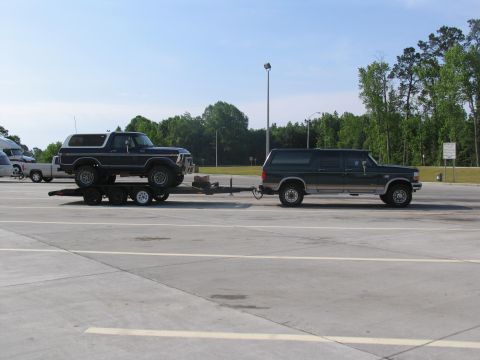 1978 Ford Bronco - A Ford Excursion tows a Ford Bronco on a trailer in a parking lot.