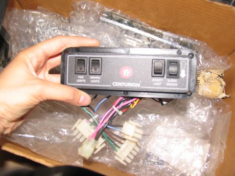 1995 Ford C-350 (Centurion Conversions) - A Centurion control panel with multiple switches and wiring harnesses is held by a hand inside a box.