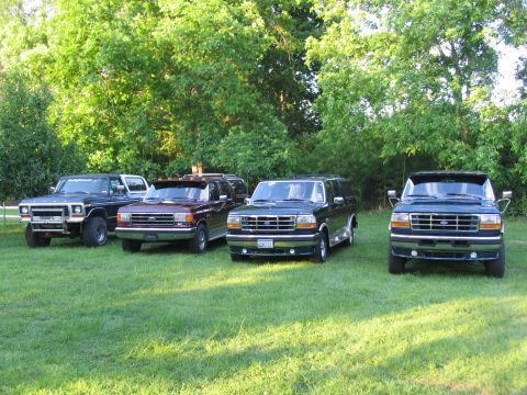 1995 Ford C-350 (Centurion Conversions) - A collection of Ford Bronco Centurion Conversions are lined up on a grassy lawn under a canopy of trees.