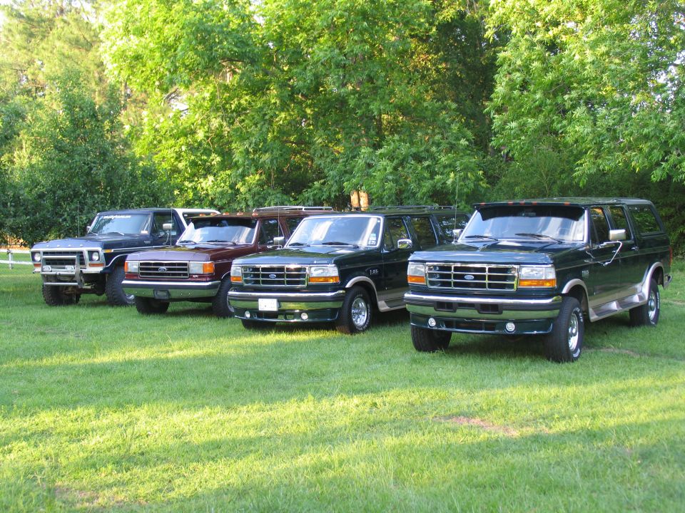 Four dark green Ford Bronco/F-Series SUVs parked on grass, with a dark blue one in the background